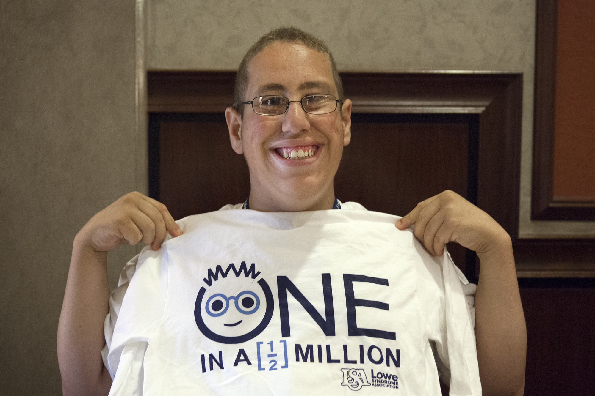 Young man with Lowe syndrome smiling while holding a conference t shirt